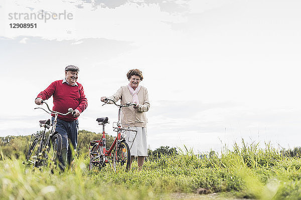 Senior couple pushing bicycles in rural landscape