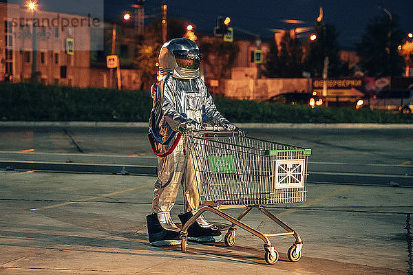 Spaceman in the city at night on parking lot with shopping cart