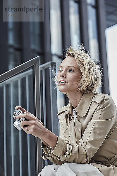 Portrait of young blond woman with digital camera sitting on stairs