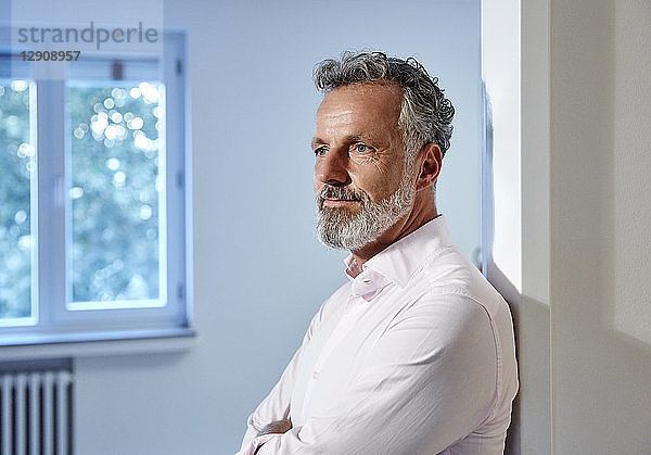 Portrait of mature man leaning against doorframe in office thinking