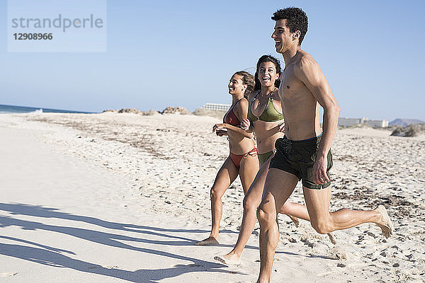 Happy carefree friends running on the beach to the sea