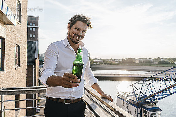 Happy businessman standing on balcony  drinking beer