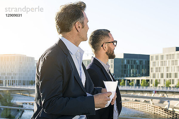 Two businessmen on a bridge in the city looking around