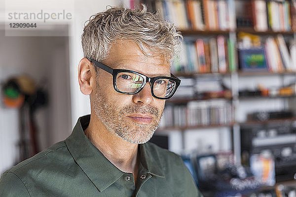 Portrait of mature man with grey hair and stubble wearing glasses at home