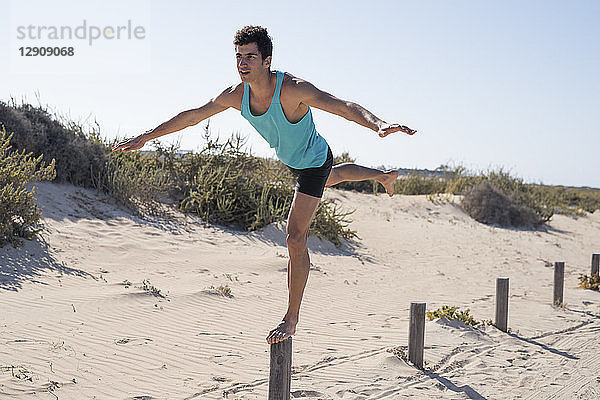 Spain  Canary Islands  Fuerteventura  young man exercising on the beach balancing on a pole