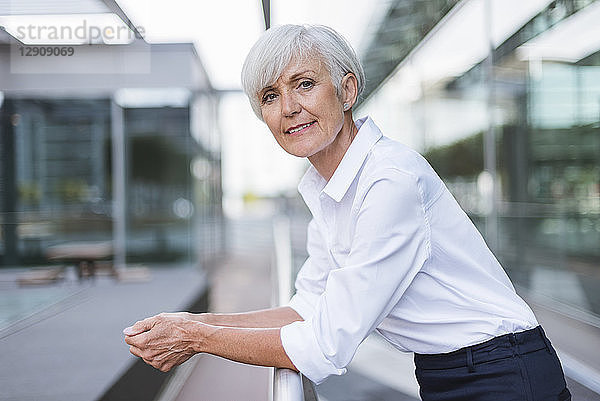 Portrait of confident senior woman leaning on railing in the city