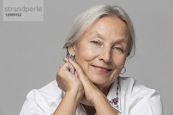 Portrait of relaxed senior woman with grey hair in front of grey background