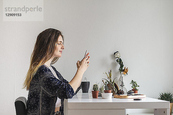 Young woman using cell phone at home surrounded by plants
