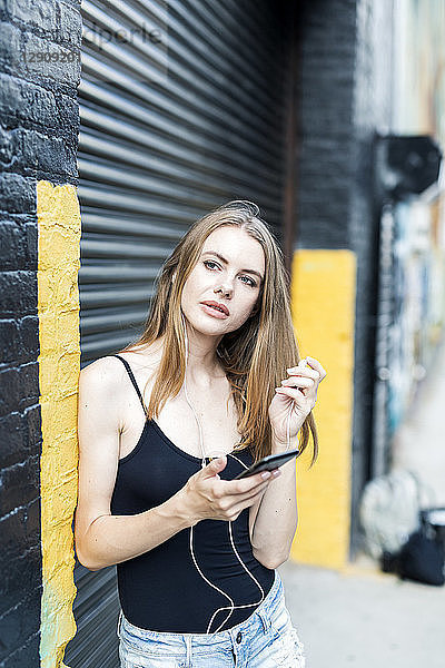 Young woman leaning on street corner  listening music  using smartphone