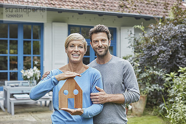 Portrait of smiling couple standing in front of their home holding house model