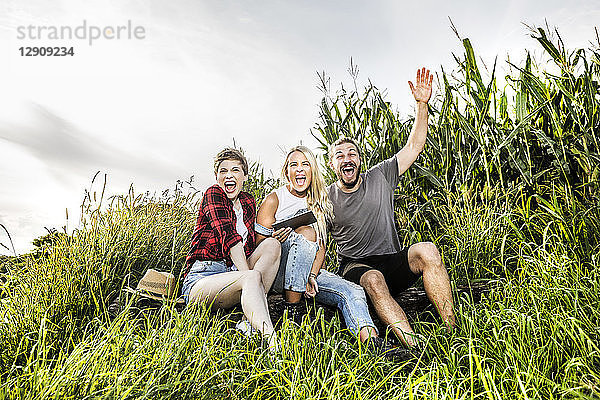 Carefree friends with tablet sitting at a cornfield
