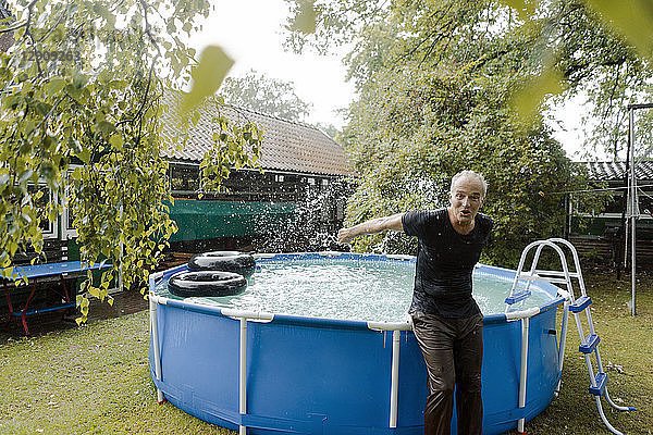 Portrait of carefree mature man enjoying summer rain at swimming pool in garden