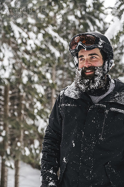Smiling young man in skiwear in winter forest looking sideways