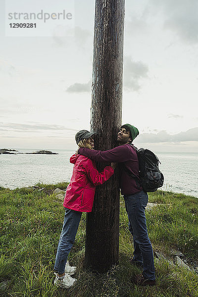 Norway  Lofoten  young couple hugging a pole at the coast