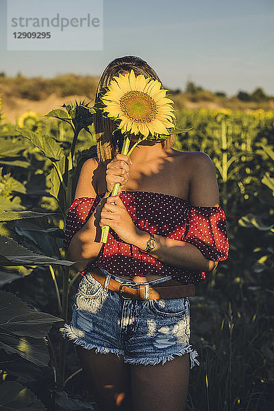 Young woman standing in a field holding a sunflower in front of her face
