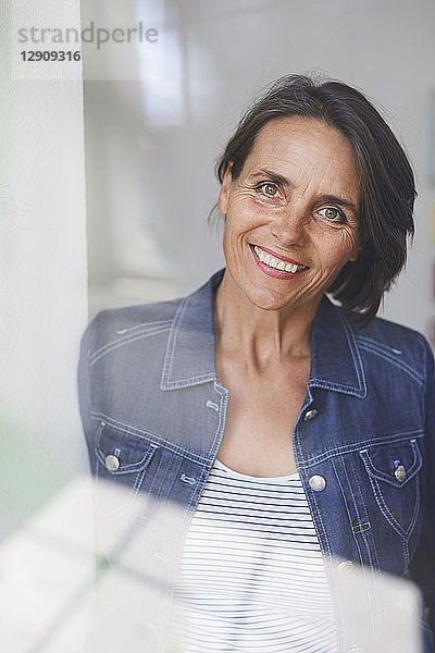 Portrait of smiling mature woman behind windowpane