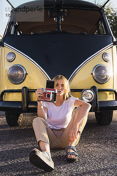 Young woman holding vintage camera sitting outside at a van