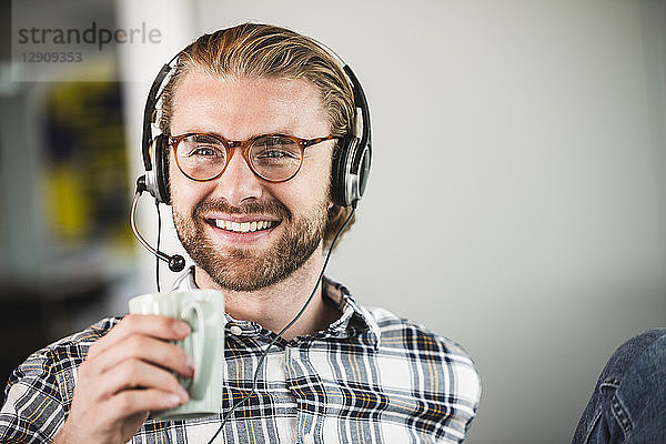 Portrait of smiling casual businessman with cup of coffee and headset