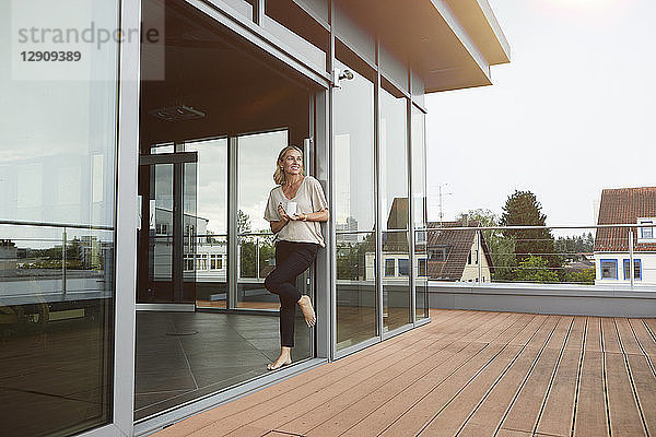 Smiling mature woman with cup of coffee standing at roof terrace at home