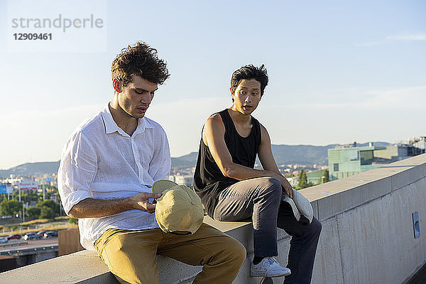 Two young men sitting and talking on a wall