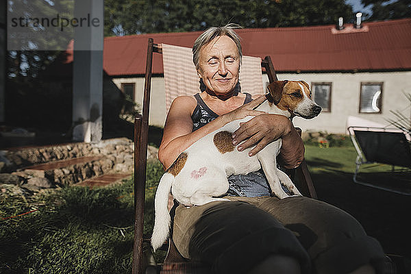 Smiling senior woman with dog on deckchair in garden