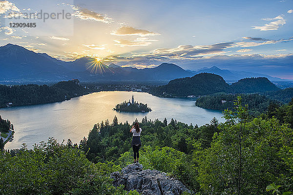 Slovenia  Bled  Young woman taking picture of Bled island and Church of the Assumption of Maria at sunrise