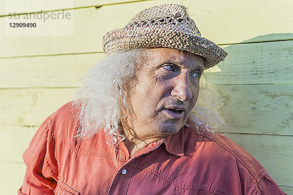 Senior man with long gray hair wearing straw hat looking sideways