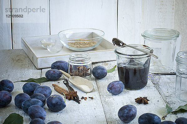 Preserving jar of plum jam and ingredients on wood