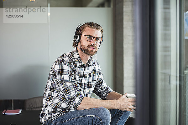 Casual businessman with cup of coffee and headset in office