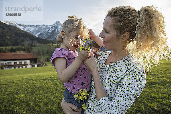 Austria  Tyrol  Walchsee  mother carrying daughter with flowers on an alpine meadow