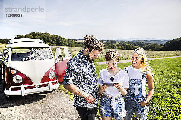 Happy friends outside van in rural landscape looking at tablet