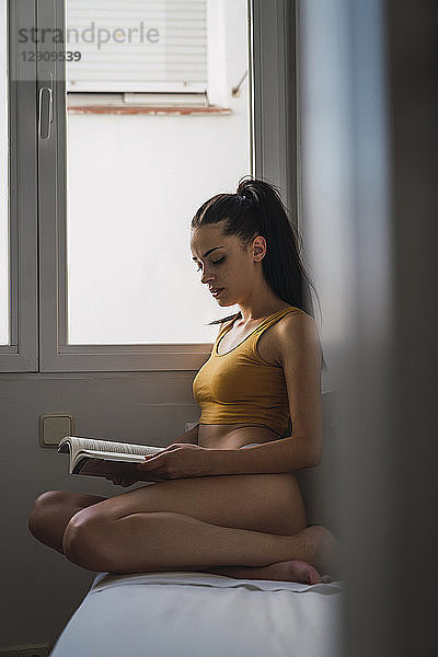 Beautiful young woman in underwear reading a book at home