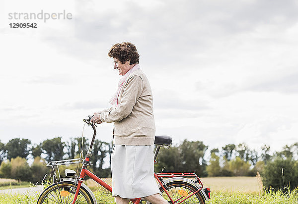 Senior woman pushing bicycle in rural landscape