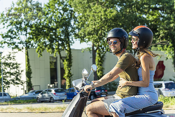 Happy couple riding motor scooter in summer