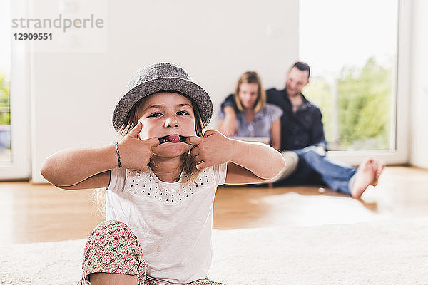 Little girl with hat having fun at home  parents using laptop in background