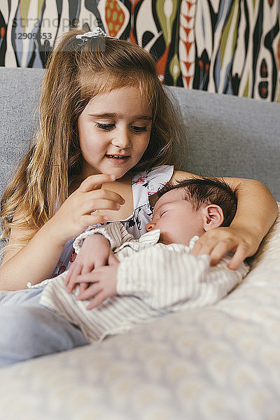 Girl sitting on couch looking at newborn baby brother