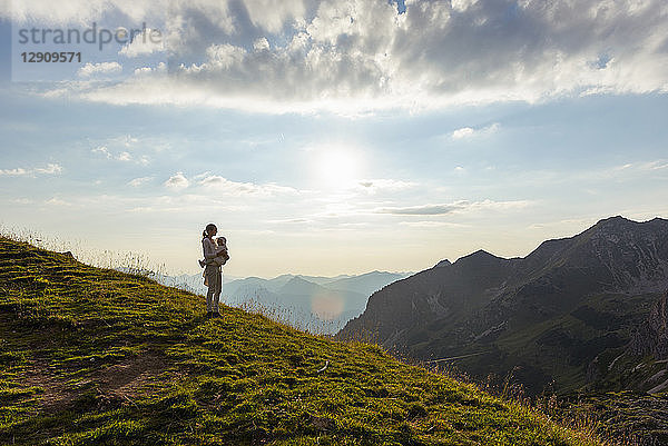 Germany  Bavaria  Oberstdorf  mother and little daughter on a hike in the mountains looking at view at sunset