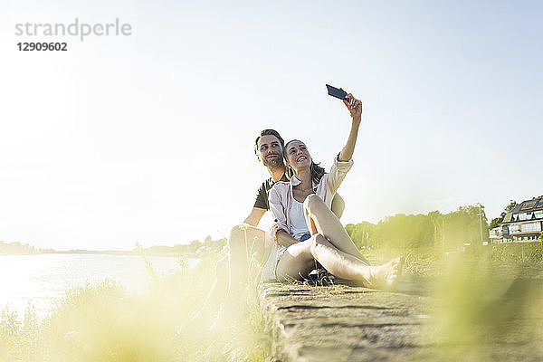 Happy couple at the riverside in summer taking a selfie