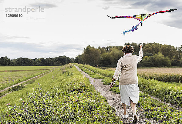Senior woman walking with kite in rural landscape