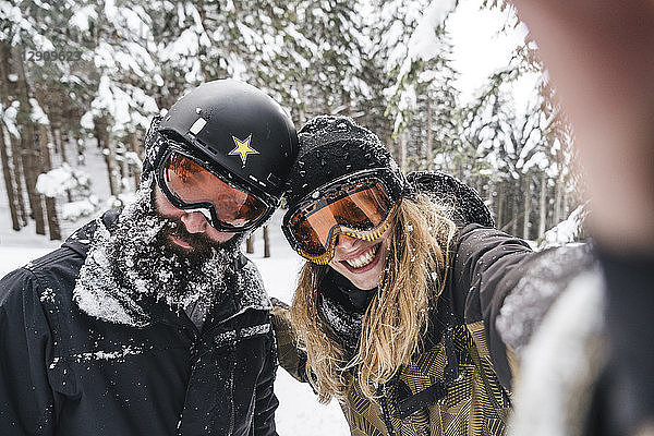 Selfie of smiling couple in skiwear in winter forest