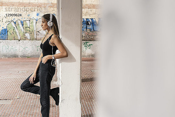 Teenage girl leaning at a column wearing headphones