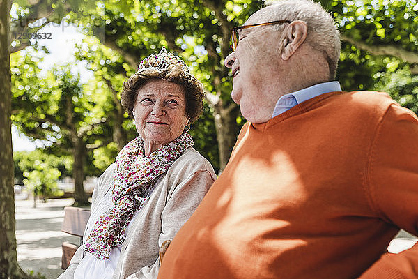 Happy senior couple sitting in park  woman wearing crown