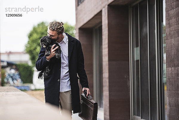 Young businessman cuddling dog outside office building