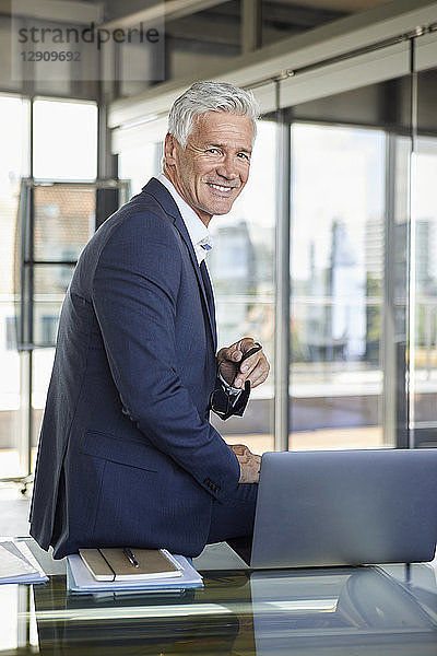 Successful manager sitting on desk  smiling