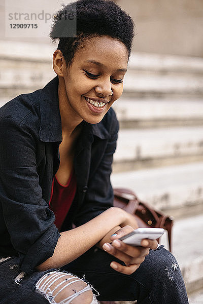 Portrait of smiling young woman sitting on stairs looking at cell phone