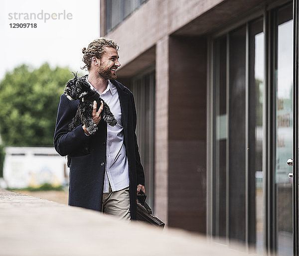 Smiling young businessman holding dog outside office building