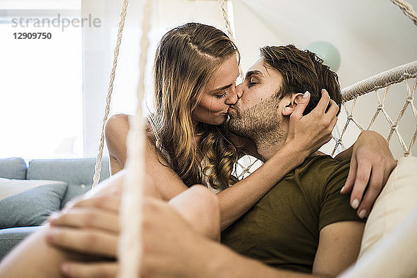Affectionate couple kissing in hanging chair at home