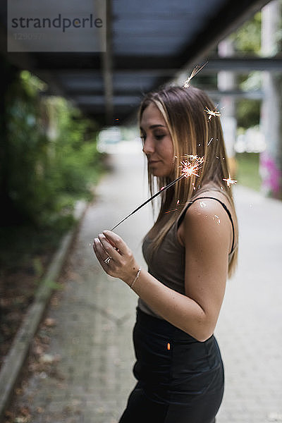 Young woman holding sparkler outdoors