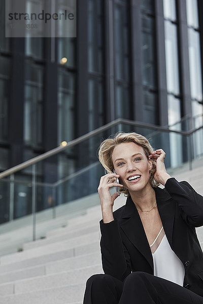 Portrait of smiling young businesswoman on the phone sitting on stairs outdoors