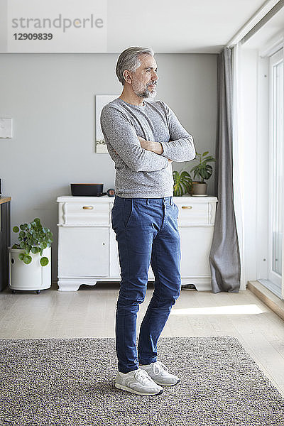 Mature man standing in his living room looking out of window